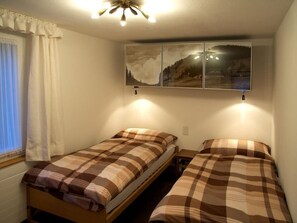 A room with two single beds, a window with curtains, a ceiling fan, and a wall-mounted artwork. - Pony 4-Bettwohnung Appartement/Fewo, Dusche oder Bad, WC, 1 Schlafraum by Interhome (Lenk)
