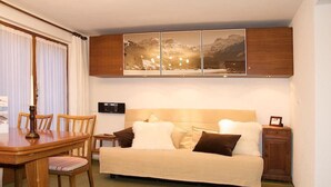 A compact hotel room with a bed, a small table, chairs, a cabinet, and a wall-mounted radio. - Pony 4-Bettwohnung Appartement/Fewo, Dusche oder Bad, WC, 1 Schlafraum by Interhome (Lenk)