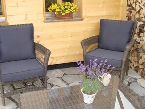 Two wicker chairs with cushions, a table with a vase of flowers, and a window with a flower box. - Gwunderstübli Appartement/Fewo, Dusche oder Bad, WC, Wohn-/Schlafraum by Interhome (Lenk)