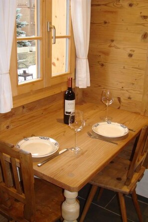 A wooden dining table with two plates, a wine bottle, and two wine glasses. - Gwunderstübli Appartement/Fewo, Dusche oder Bad, WC, Wohn-/Schlafraum by Interhome (Lenk)