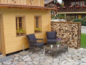 A wooden building with two windows, a glass table, and two wicker chairs. - Gwunderstübli Appartement/Fewo, Dusche oder Bad, WC, Wohn-/Schlafraum by Interhome (Lenk)