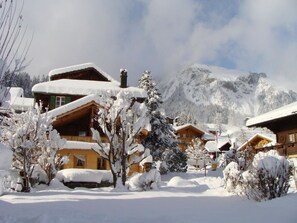 Ein verschneites Bergdorf mit Holzhäusern und einem markanten Berg im Hintergrund.
