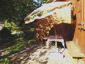 Eine Holzterrasse mit Tisch, Bank, Sonnenschirm und einem Holgebäude im Hintergrund.