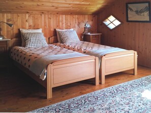 A double bed with a wooden frame, two nightstands, a lamp, a small table, and a patterned rug.