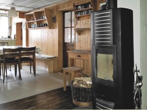 A wooden interior with a dining table, chairs, a fireplace, and shelves with kitchenware.
