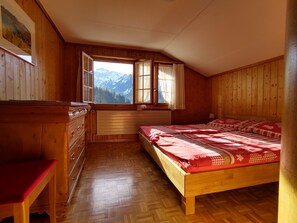 A wooden room with a bed, a dresser, a window with a mountain view, and a herringbone-patterned floor. - Bärnermutz # 2 Appartement/Fewo, Dusche oder Bad, WC, 2 Schlafräume by Interhome (Lenk)