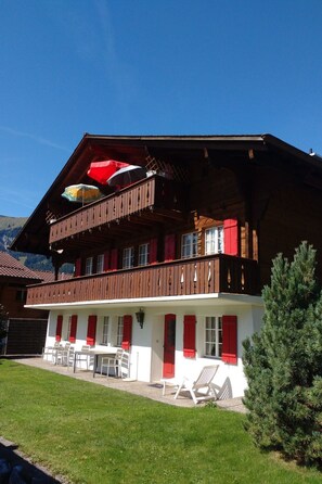 A two-story building with a balcony, outdoor seating area, and a mountain backdrop. - Bärnermutz # 2 Appartement/Fewo, Dusche oder Bad, WC, 2 Schlafräume by Interhome (Lenk)