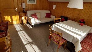 Ett mysigt rum med ett träpanelat tak, en vit soffa med röda kuddar, ett litet bord med en vit duk och en stol med en randig kudde.