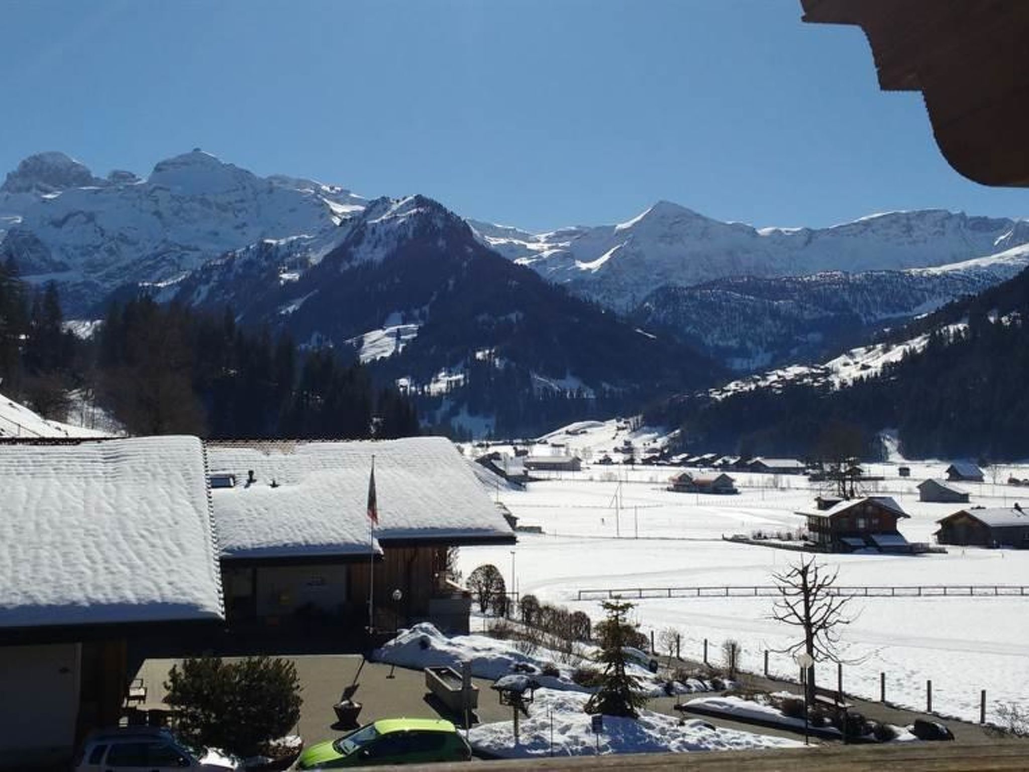 Un paysage de montagne avec des sommets enneigés et une zone résidentielle avec des maisons et des voitures garées.
