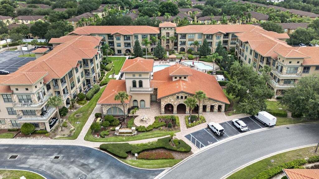 A multi-story hotel with a central courtyard, parking area, and a swimming pool.