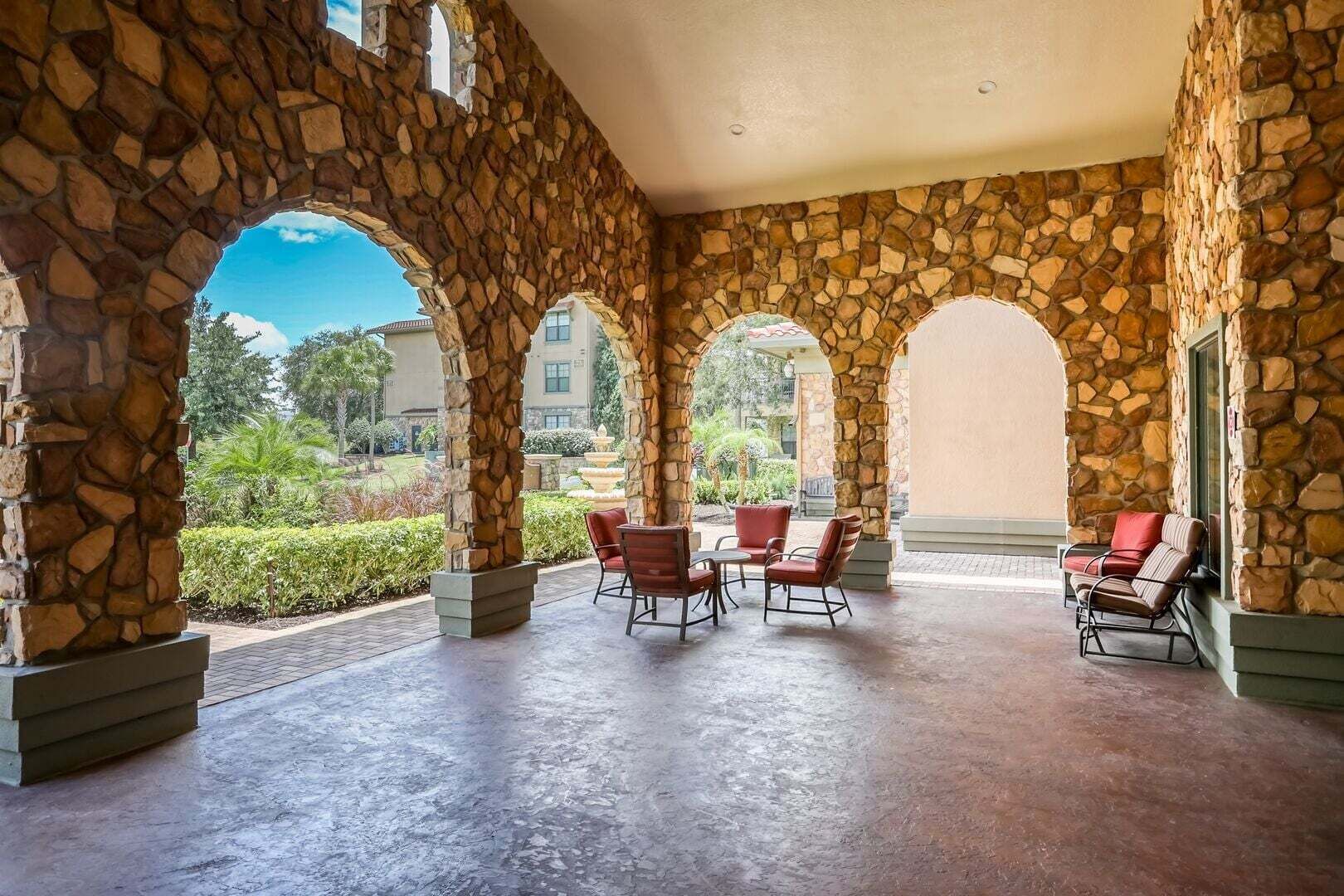 A covered outdoor area with stone walls, multiple seating arrangements, and a view of greenery and buildings in the distance.