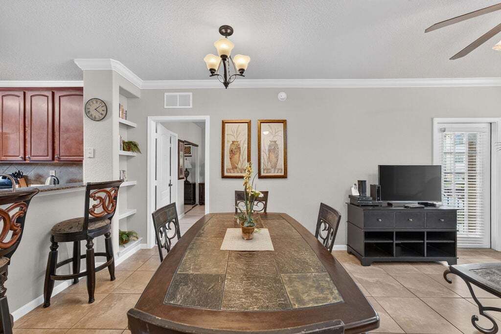 A dining area with a wooden table, chairs, a chandelier, and a television in the background.