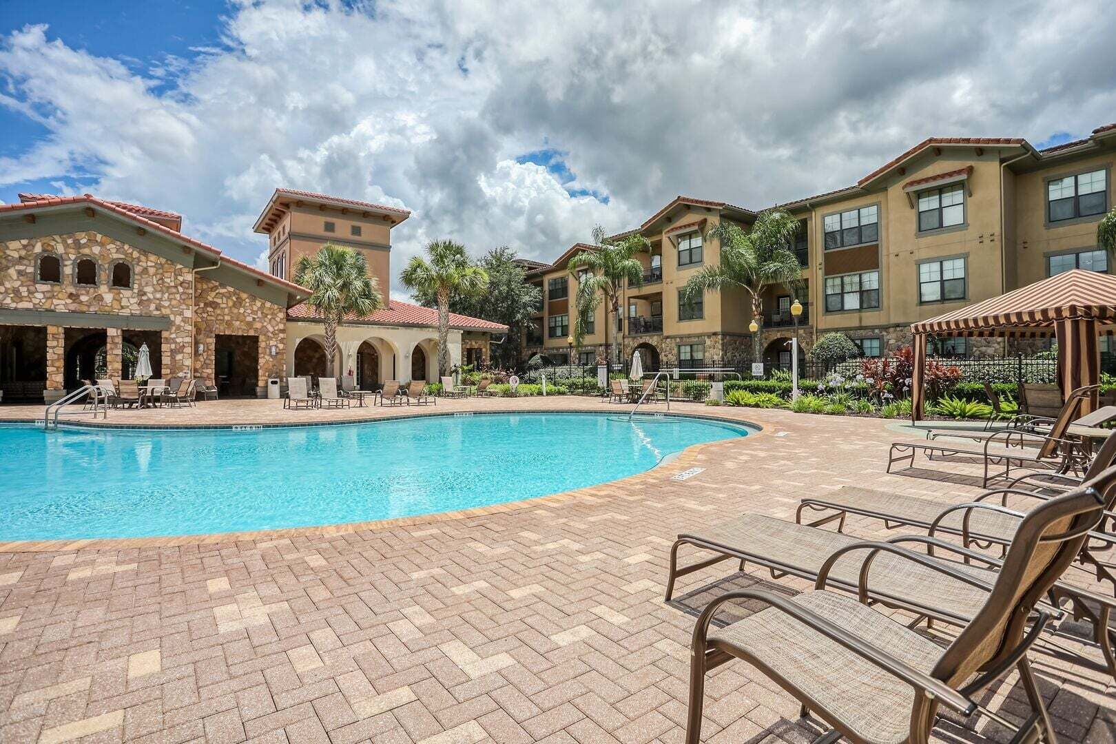 A hotel pool area with a clear blue pool, lounge chairs, and a brick patio.