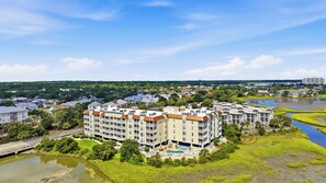 A multi-story hotel with a swimming pool and a view of a river. - Windy Hill Getaway | 3BR at Ocean Marsh (North Myrtle Beach)