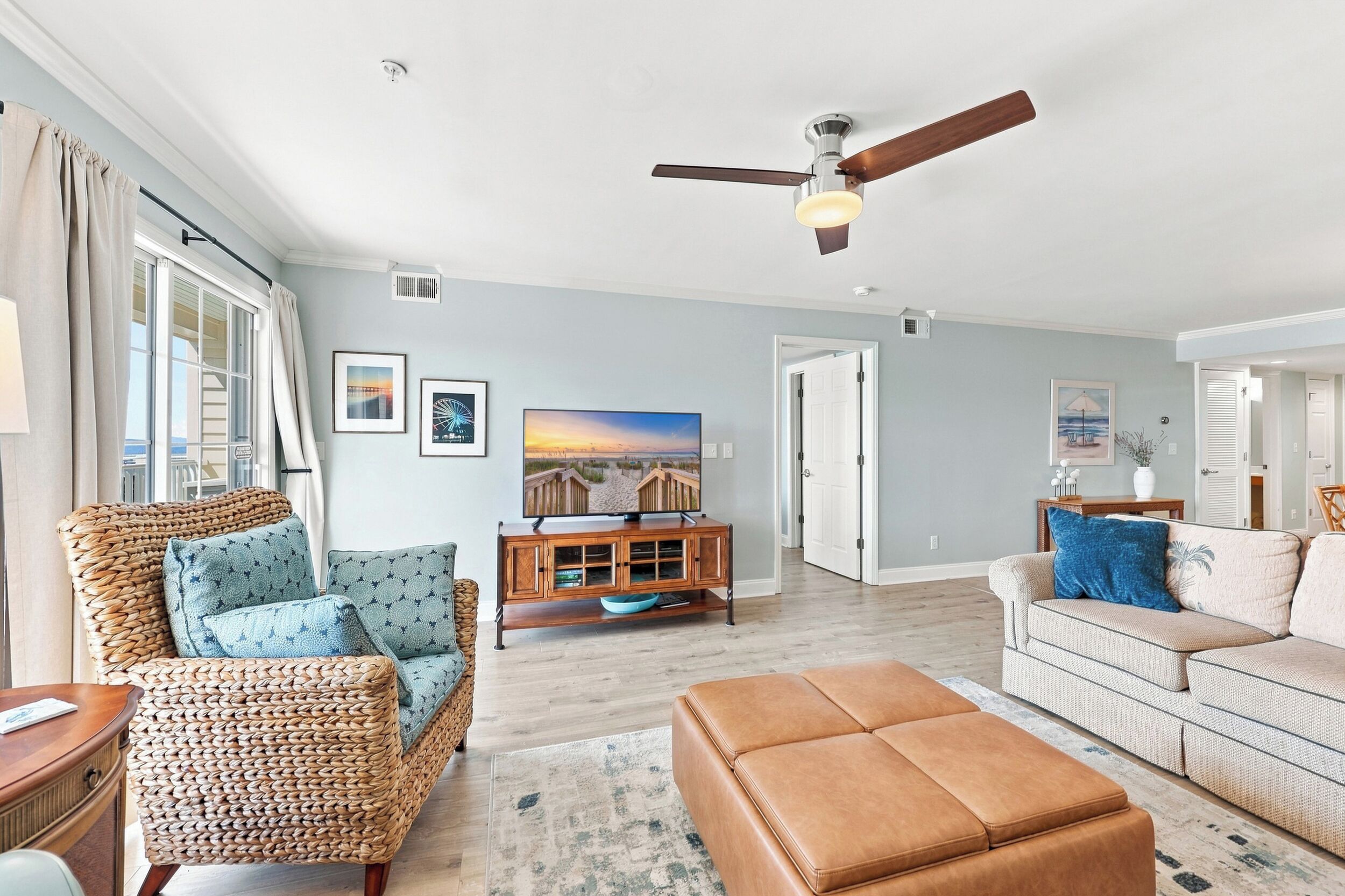 A living room with a ceiling fan, a television, wicker furniture, and a light-colored sofa.