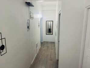 Un couloir étroit avec un plancher en bois, des murs blancs et une porte au fond.