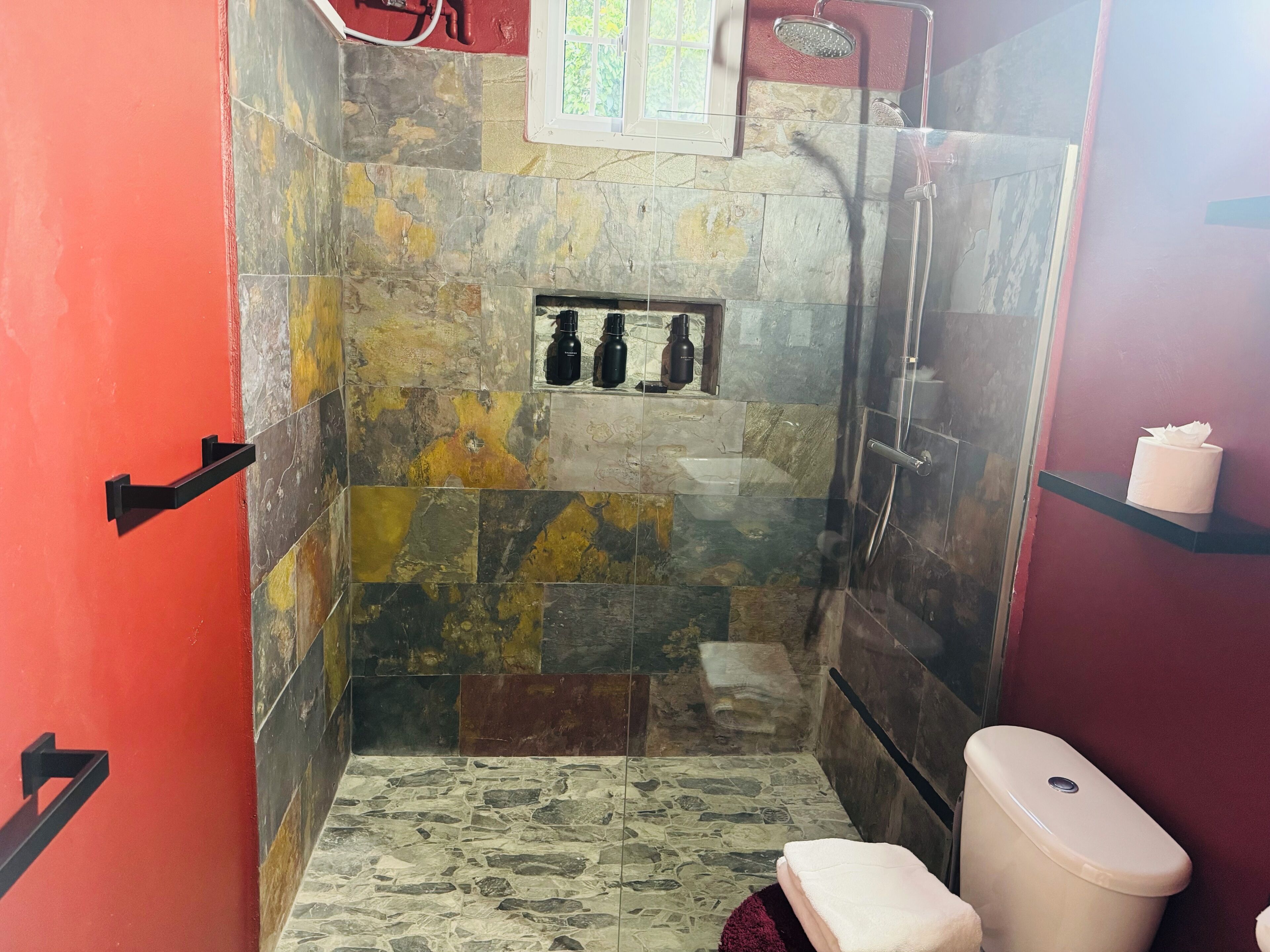 A bathroom with a shower, toilet, and a shelf with toiletries.