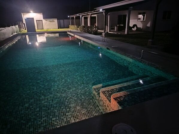Une piscine nocturne à l’eau claire, entourée d’un patio abrité.