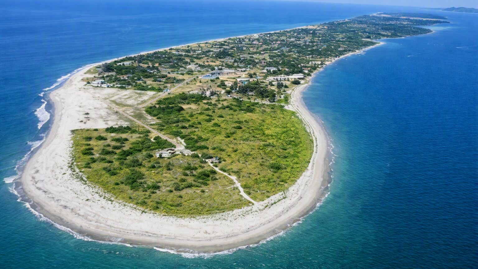 Une vue aérienne d’une propriété située sur la côte, avec une plage, une route menant à la plage et un ensemble de bâtiments.