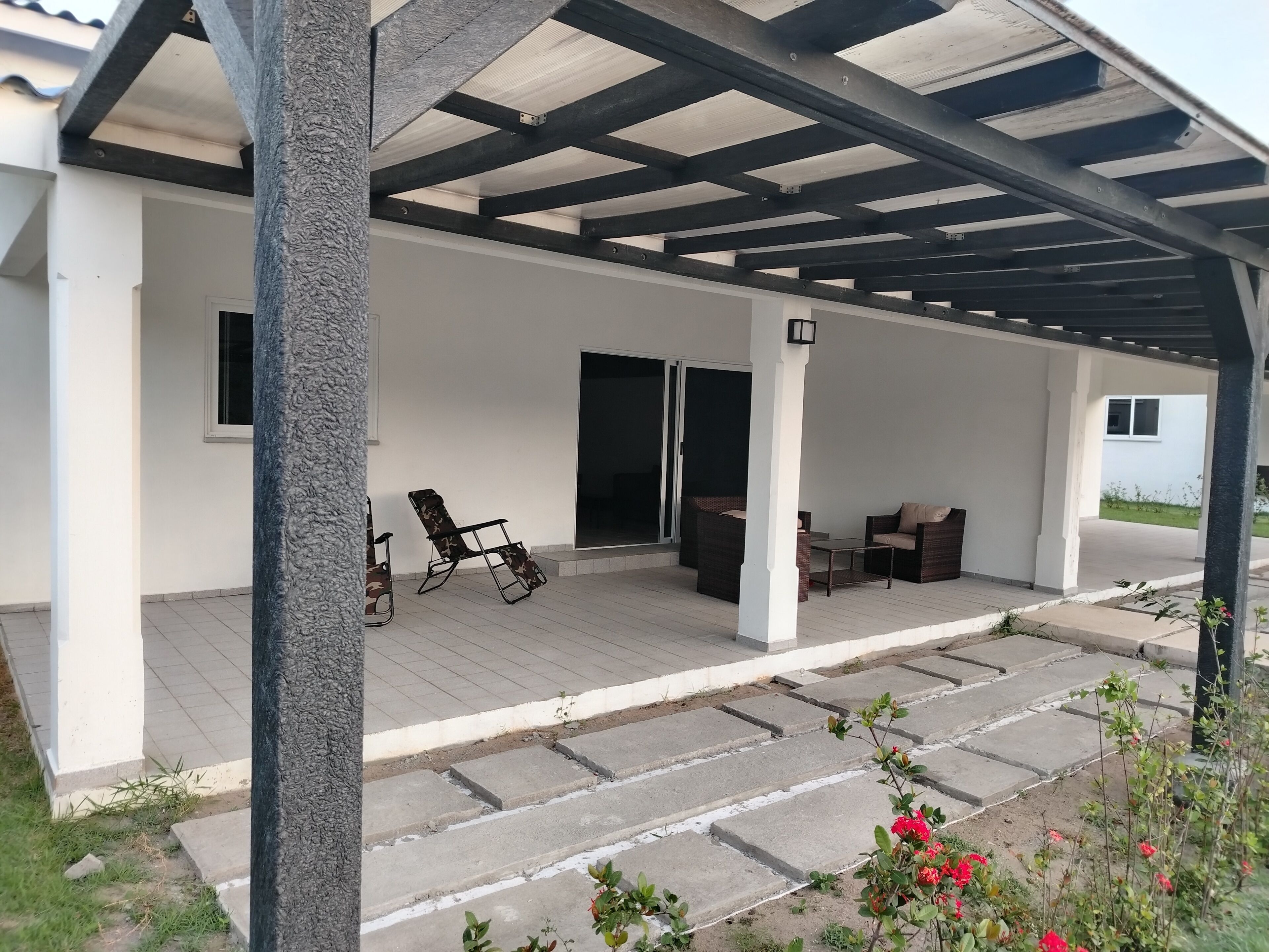 Une terrasse extérieure couverte, dotée d’un espace salon, d’une table et d’une porte-fenêtre coulissante donnant sur un espace intérieur.