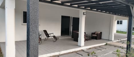 A covered outdoor patio with a seating area, a table, and a sliding glass door leading to an interior space.