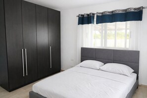 Quarto com cama, guarda-roupa e janela com cortinas.