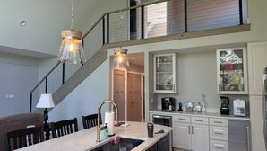 A modern kitchen with a marble countertop, stainless steel appliances, and a mezzanine with a balcony. - NEW Kenai Cabin with Modern Interior and Cabin Exterior (Soldotna)