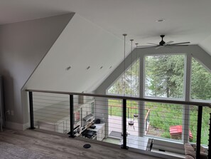 Ein modernes Interieur mit schrägen Wänden, einem Balkon mit Blick auf Grünflächen und einem Essbereich mit Gartenmöbeln.