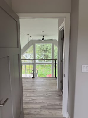 A hallway leading to a covered outdoor area with a ceiling fan, a view of a green landscape, and a wooden floor. - NEW Kenai Cabin with Modern Interior and Cabin Exterior (Soldotna)