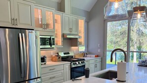 A modern kitchen with stainless steel appliances, a large island, and a view of the outdoors. - NEW Kenai Cabin with Modern Interior and Cabin Exterior (Soldotna)