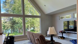 A spacious room with large windows, a sofa, a table, and a lamp. - NEW Kenai Cabin with Modern Interior and Cabin Exterior (Soldotna)