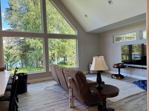 A spacious room with large windows, a sofa, a table, and a lamp.
