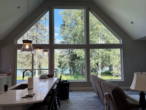A spacious room with a large window, a kitchen area, and a seating area. - NEW Kenai Cabin with Modern Interior and Cabin Exterior (Soldotna)