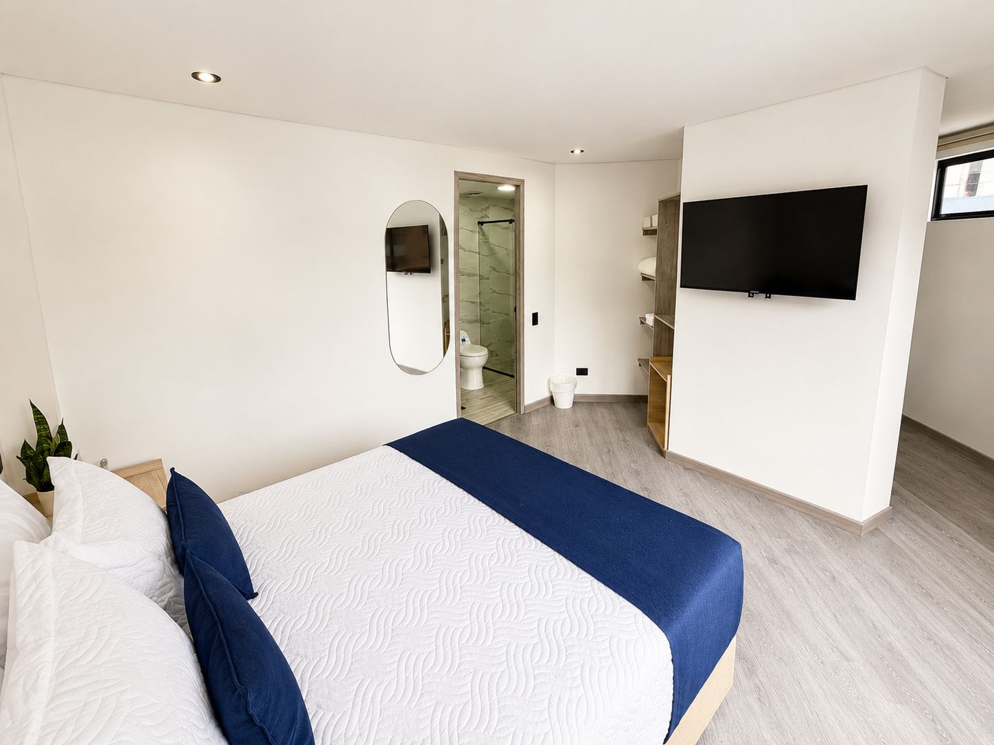 A modern hotel room with a large bed, a flat-screen TV mounted on the wall, and a bathroom visible through an open door.