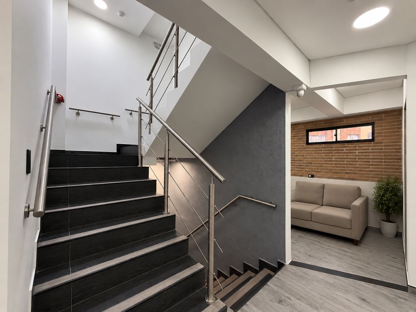 A modern interior with a staircase, a sofa, and a potted plant.