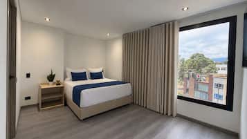 Un dormitorio moderno con una cama grande, una mesita de noche con una planta y vistas a la ciudad a través de un amplio ventanal.