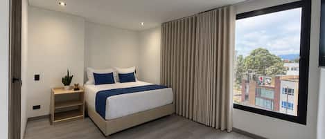 Un dormitorio moderno con una cama grande, una mesita de noche con una planta y vistas a la ciudad a través de un amplio ventanal.