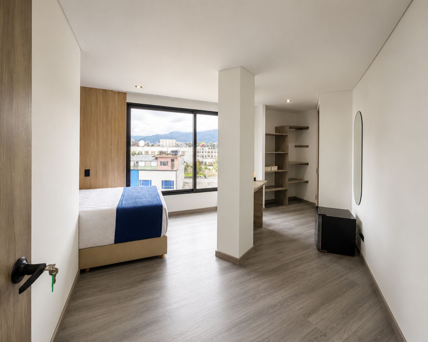 A modern bedroom with a bed, a wardrobe, and a view of the city through a large window.