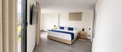 A modern bedroom with a large bed, a television mounted on the wall, and a window with curtains.