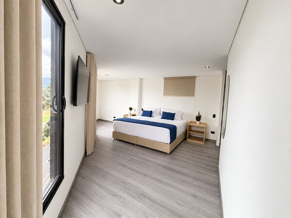 A modern bedroom with a large bed, a television mounted on the wall, and a window with curtains. - Hotel Embajada 47 (Bogota)