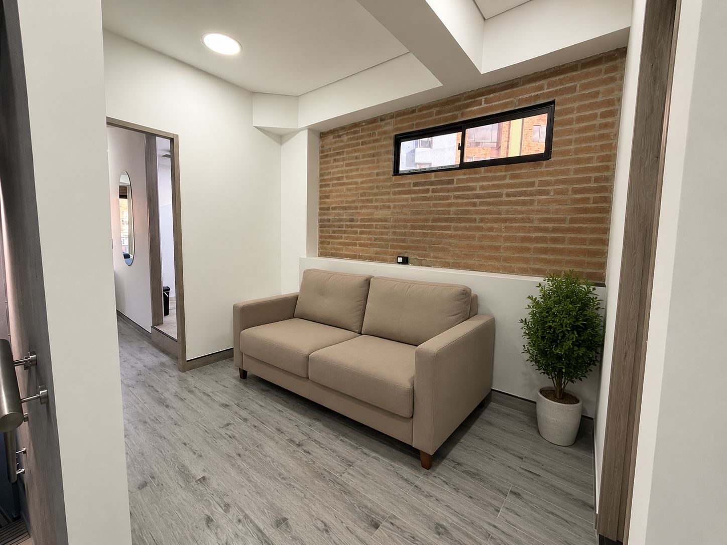 Un interior moderno con un sofá color beige, una planta en maceta y una pared de ladrillo.