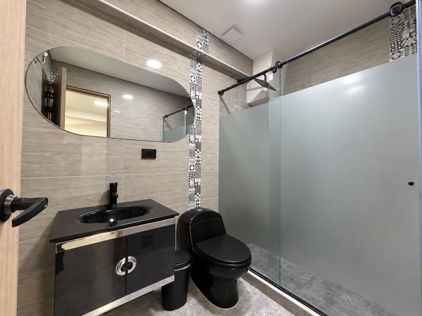A modern bathroom with a black vanity, a toilet, and a glass shower enclosure.