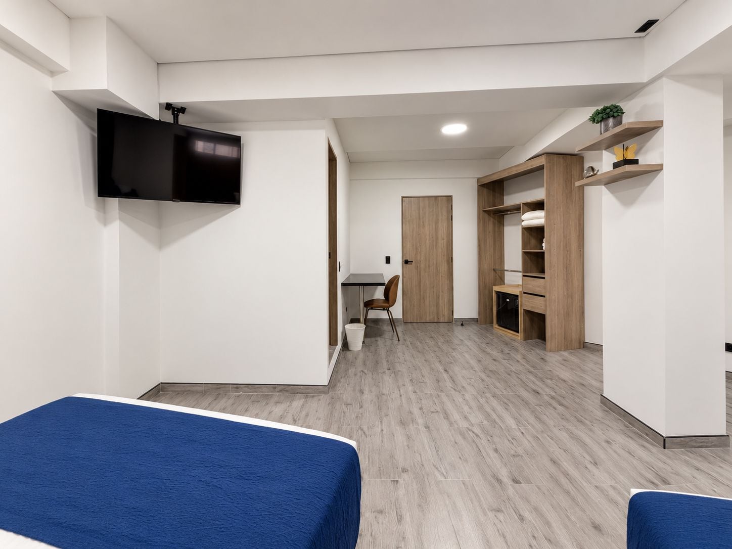 A modern, minimalist room with a bed, a TV mounted on the wall, a desk, and a wardrobe.