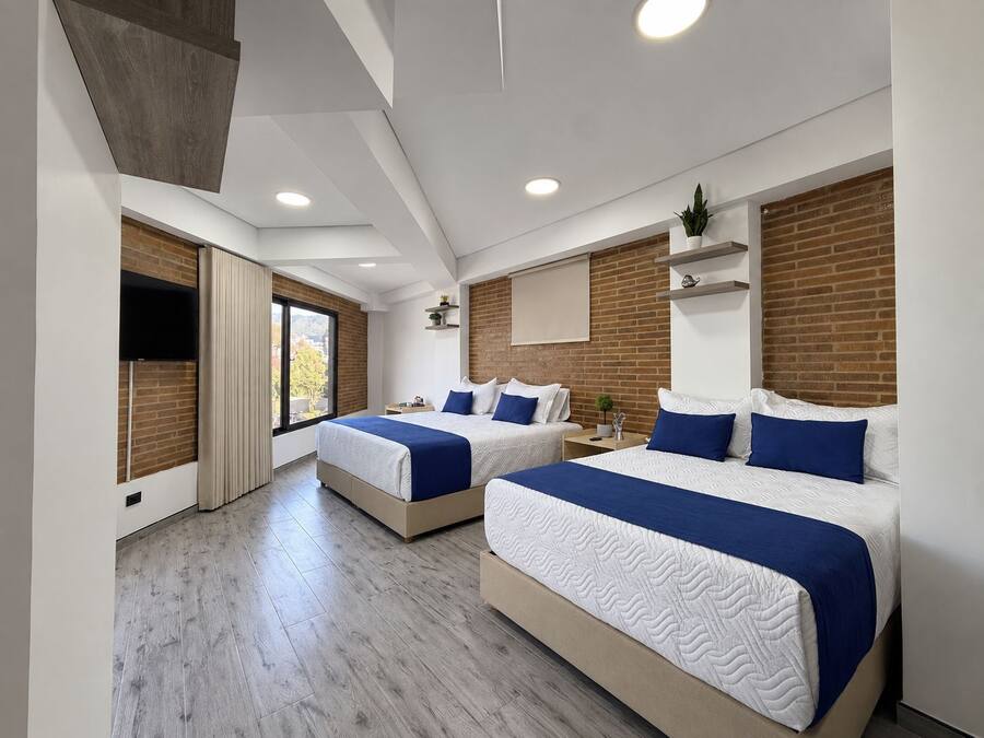 A modern hotel room with two beds, a large window, and a brick accent wall.