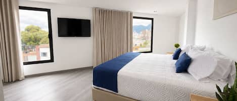 A modern hotel room with a large bed, a flat-screen TV, and a city view.