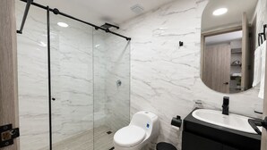 Un baño moderno con ducha acristalada, inodoro, lavabo y espejo.