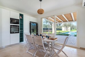 A modern kitchen with built-in appliances and a dining area with white chairs and a table, overlooking a swimming pool. - Villa Fedalì With Pool, Francavilla Fontana, Italy (Francavilla Fontana)