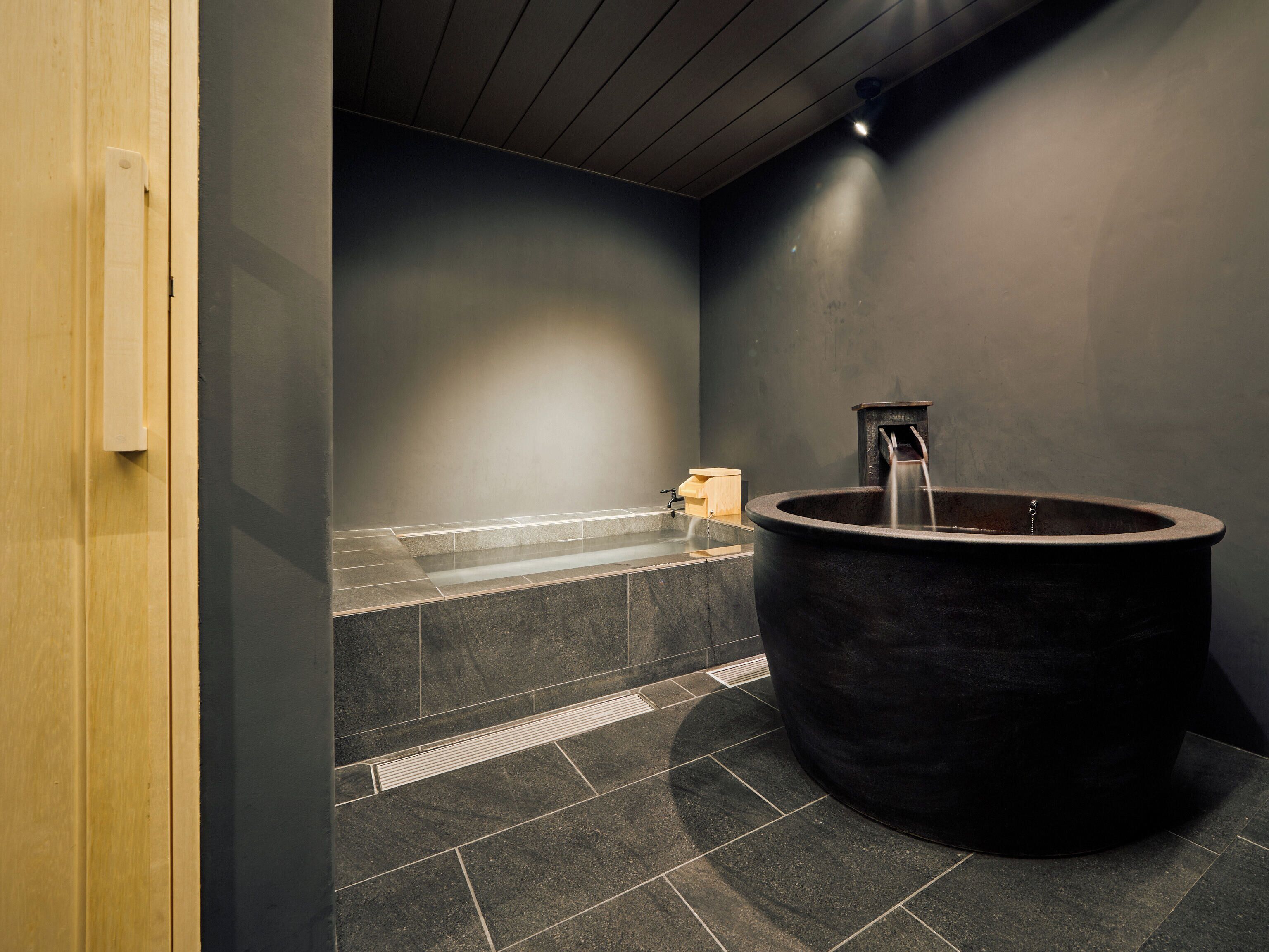 Een moderne badkamer met een groot zwart bad, een houten deur en een betegelde vloer.