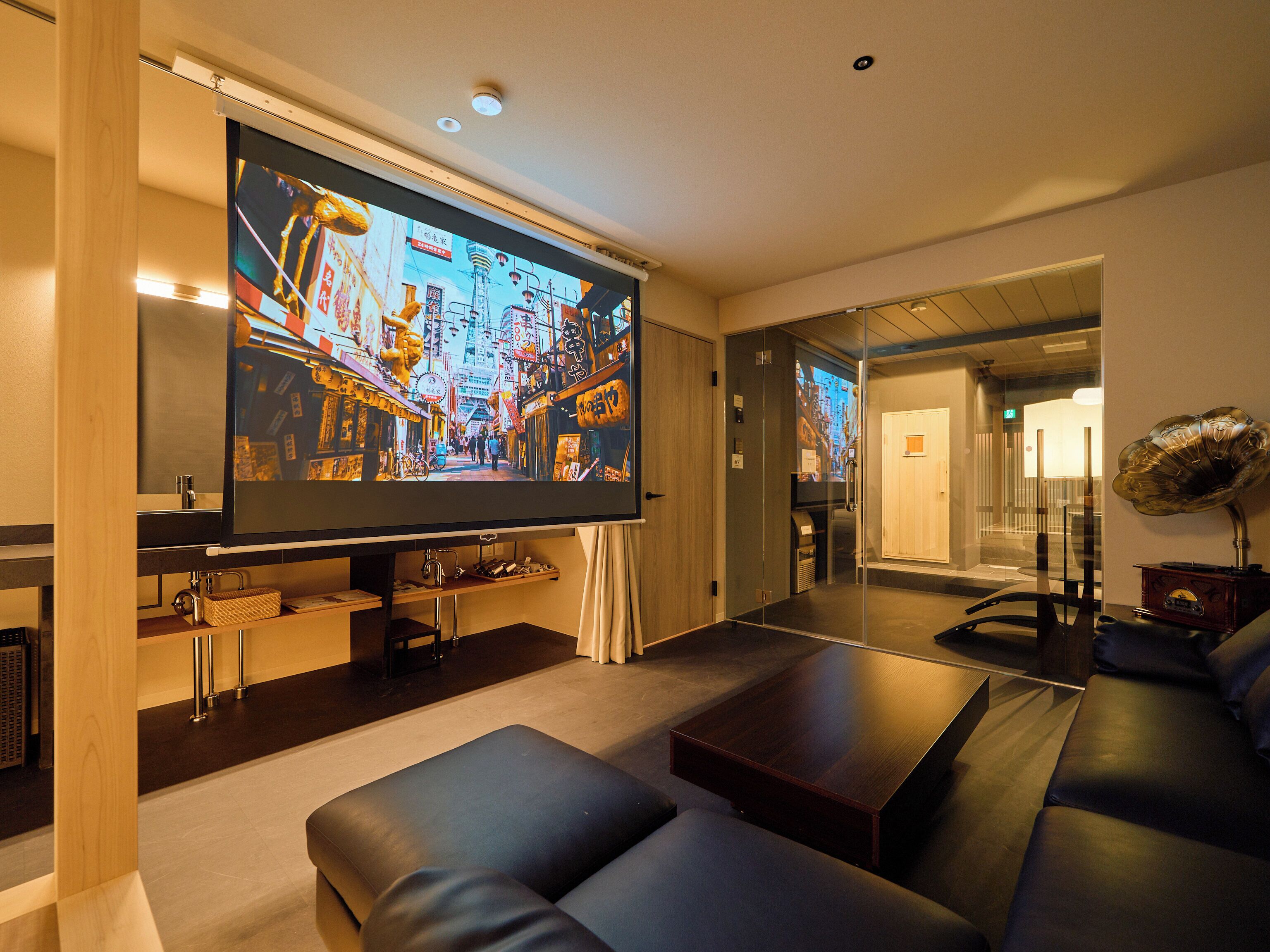 A modern living room with a large flat-screen TV, leather sofas, a coffee table, and a decorative gramophone.