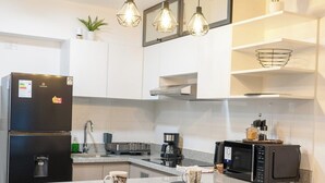 Eine moderne Küche mit integrierter Kochinsel, Barhocker, einem Kühlschrank, einer Mikrowelle und Pendelleuchten.